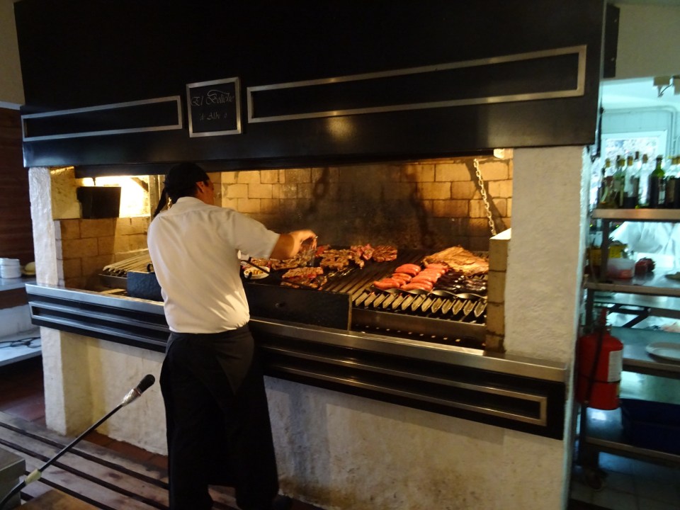 A chef at a Parilla cooking meat over a wood fire
